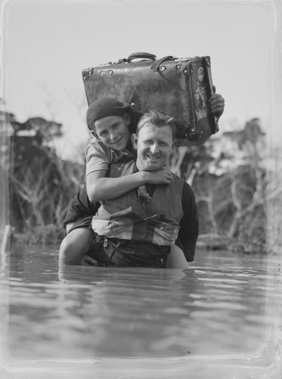 A_man_carries_a_child_across_a_body_of_water_(AM_87661-1)